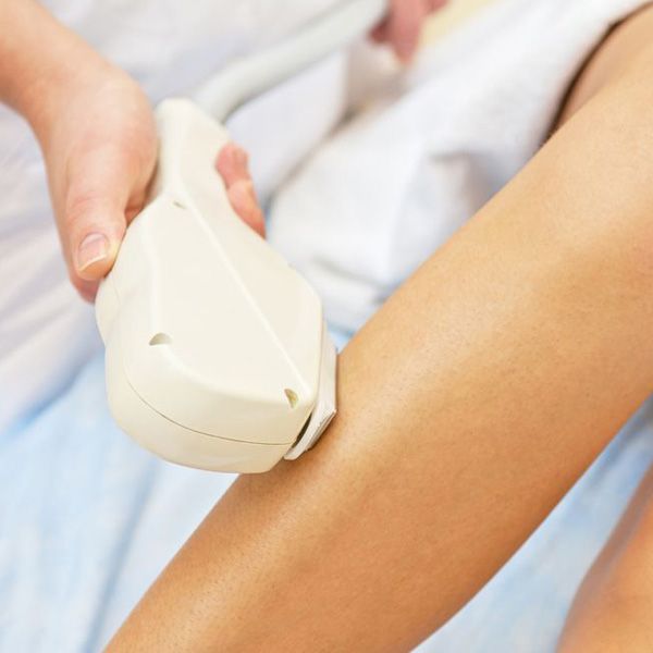 Una mujer que lleva una toalla blanca se sienta en el suelo con una rodilla doblada y las manos en la parte inferior de la pierna.