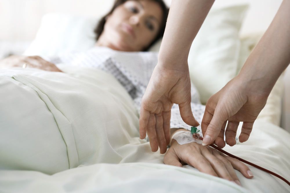 Woman lying in hospital bed as an IV is put in her hand.