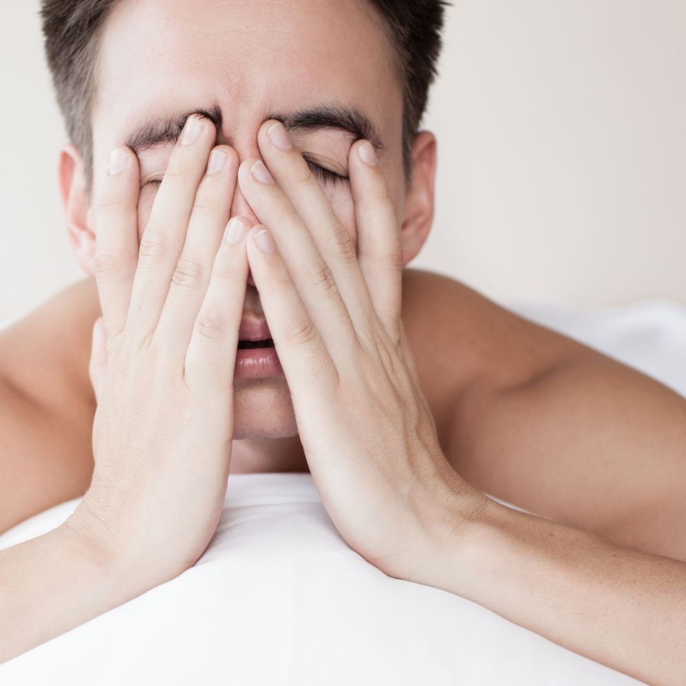 Frustrated man laying in bed and holding face in hands