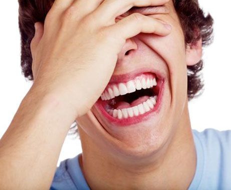 A young man laughing with his hand covering his eyes.