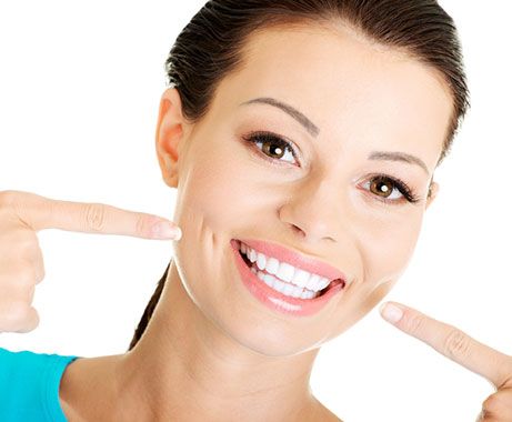 A young woman with brown hair smiling and pointing at her teeth.