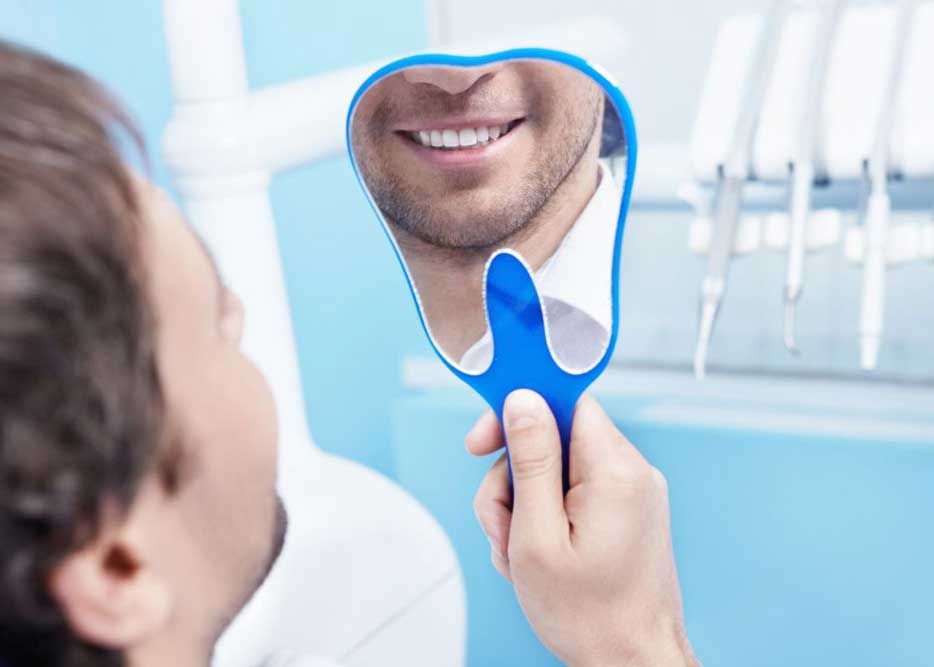 A man smiling into a tooth-shaped mirror