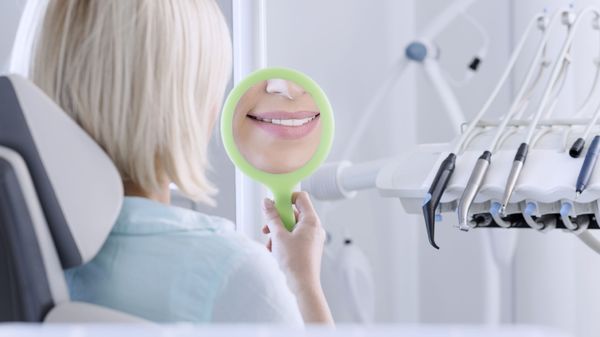 A woman smiling into a handheld mirror.