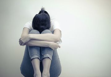 A depressed woman sits alone with her head buried between her knees