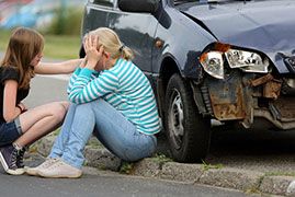 Distraught woman sitting beside a car after an accident