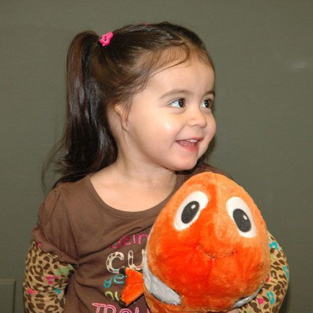 Cute little girl with misshapen ear holding fish plush