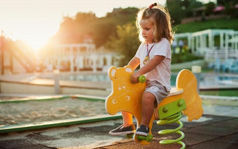 A young child sits unsupervised on a toy horse in a playground