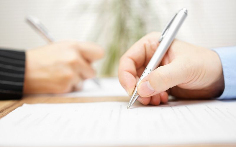 A close up shot of a couple's hands as they each sign a prenuptial agreement