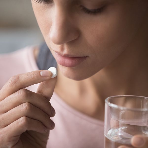 Woman holding glass and raising pill to mouth