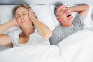 A woman covers her ears while her partner snores loudly
