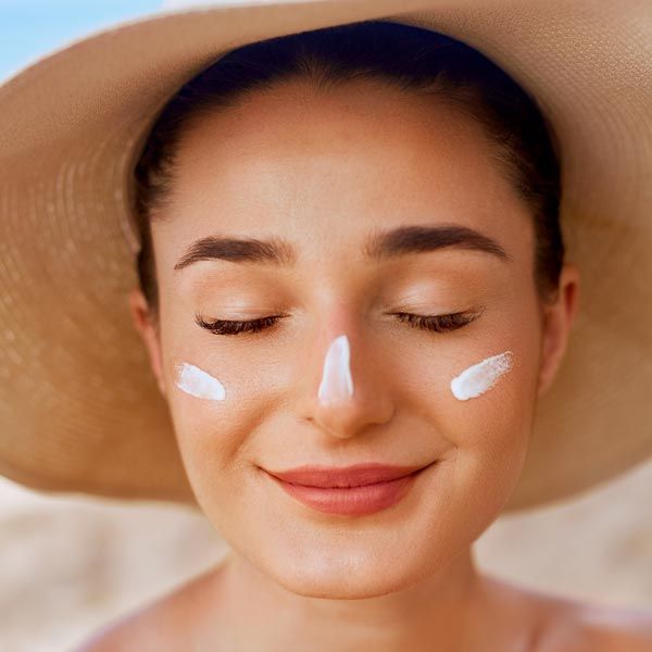 Close up of a woman with eyes closed wearing a sunhat and sunscreen on her nose and cheeks