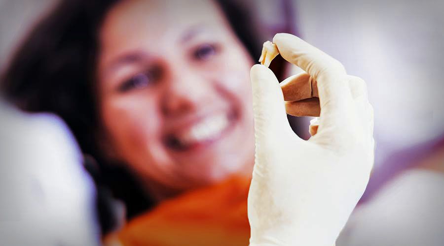 A dentist holds up a tooth in his hand while a woman smiles in the background