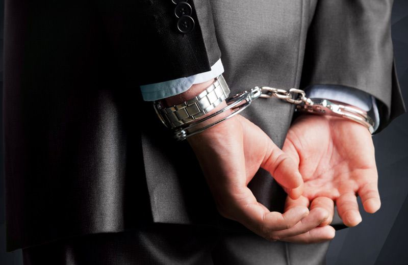 Person in business suit with hands cuffed