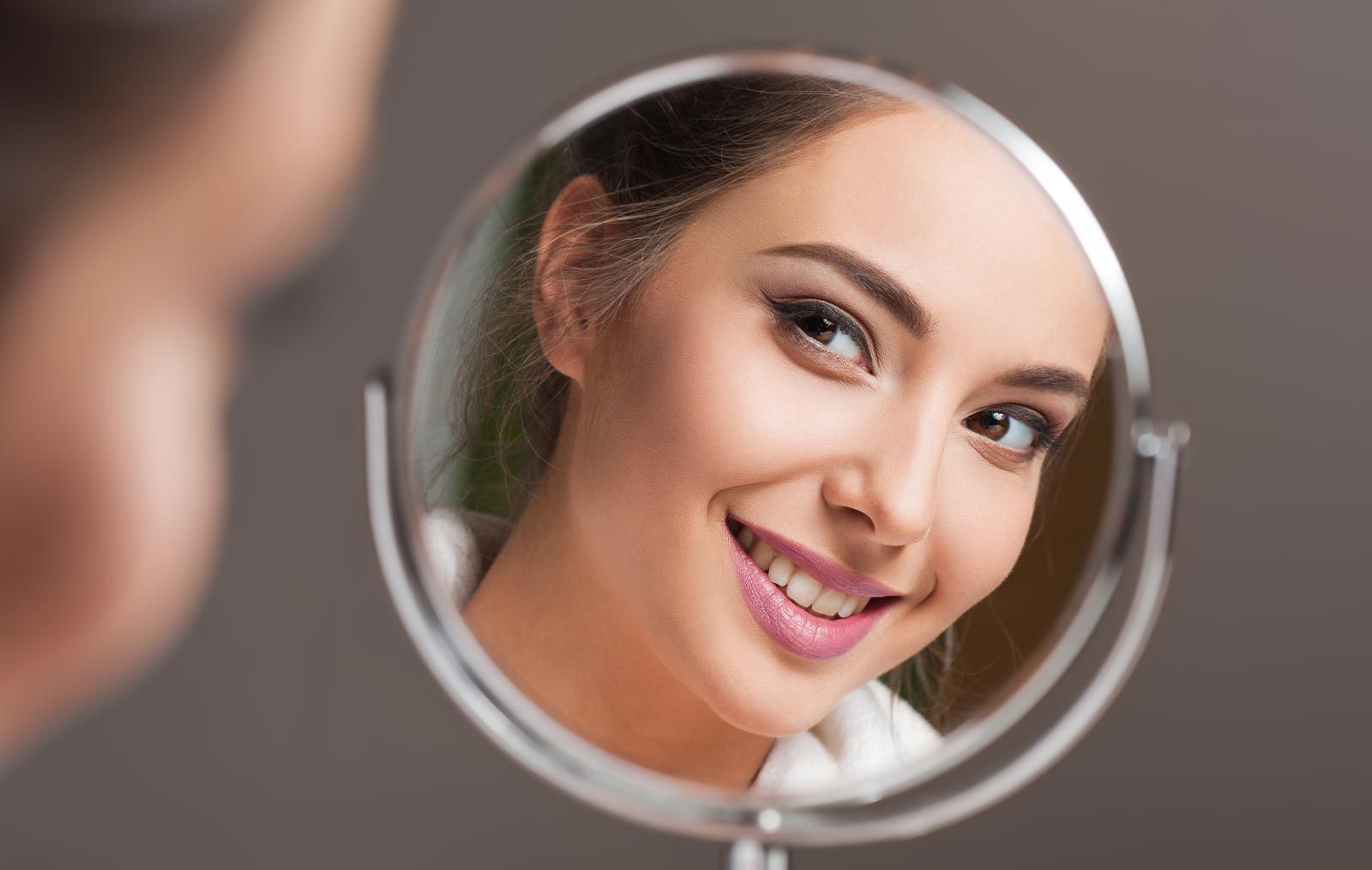 Young woman smiling into hand mirror
